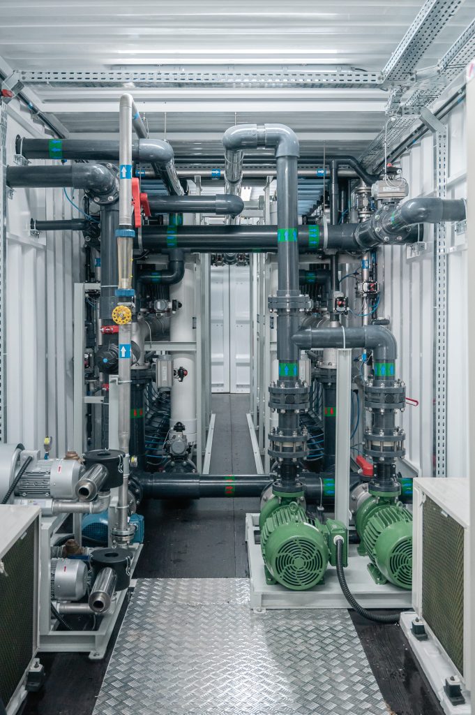 Interior do sistema de ultrafiltração industrial com tubulações, válvulas, bombas centrífugas verdes e estrutura modular para tratamento de água