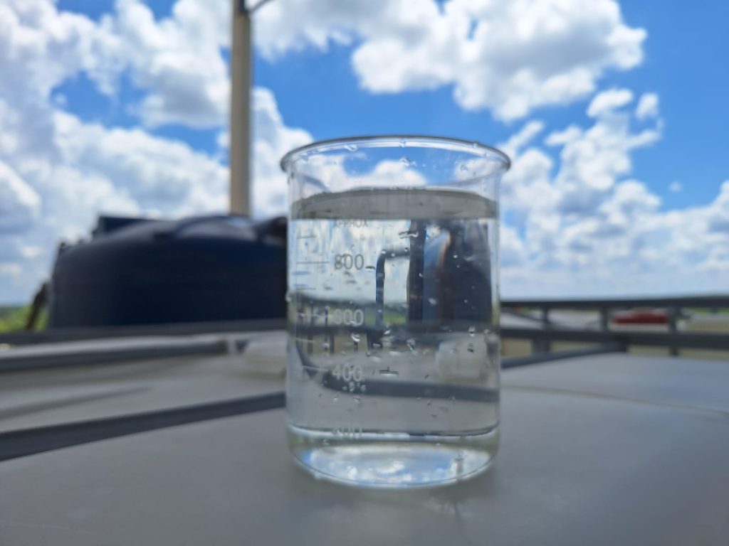 Béquer de laboratório com água cristalina e transparente, resultado do tratamento físico-químico realizado pela ETA desenvolvida pela TEGA Engenharia em Porto Feliz-SP, com céu azul ao fundo.